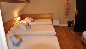 Et hotelværelse med tre enkeltsenge, trægavle, en radiator ophængt på væggen og træpynt på væggen.