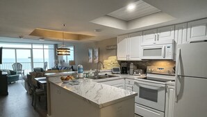 Une cuisine moderne avec des meubles blancs, un îlot en marbre et une vue sur le salon.