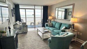 Un salon comprenant un canapé, des fauteuils, une table basse et offrant une vue sur l’océan grâce à de grandes fenêtres.