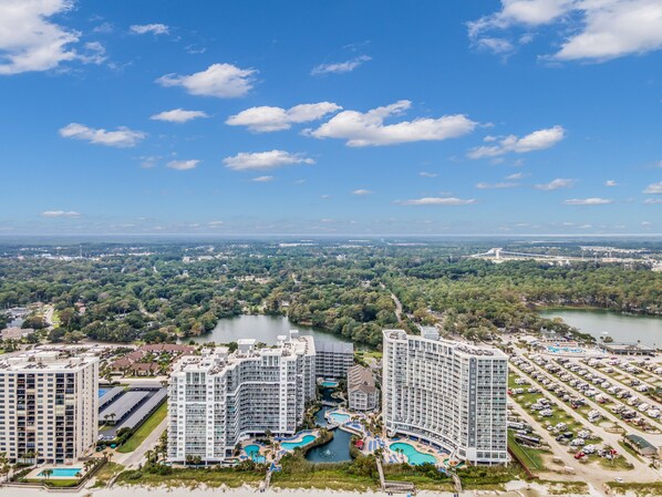 Un hotel moderno de gran altura con varios balcones, un área de piscina central y vistas a un río y follaje circundante.