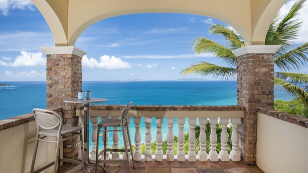 A balcony with a view of the ocean, featuring a table and chairs, and a brick pillar. - Private Villa*MagensBay *Ocean front* Private Pool (St. Thomas)
