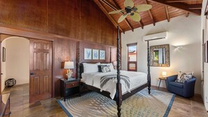 A spacious bedroom with a four-poster bed, wooden ceiling beams, and a large window. - Private Villa*MagensBay *Ocean front* Private Pool (St. Thomas)