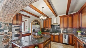 A spacious kitchen with granite countertops, wooden cabinets, and a stone archway. - Private Villa*MagensBay *Ocean front* Private Pool (St. Thomas)