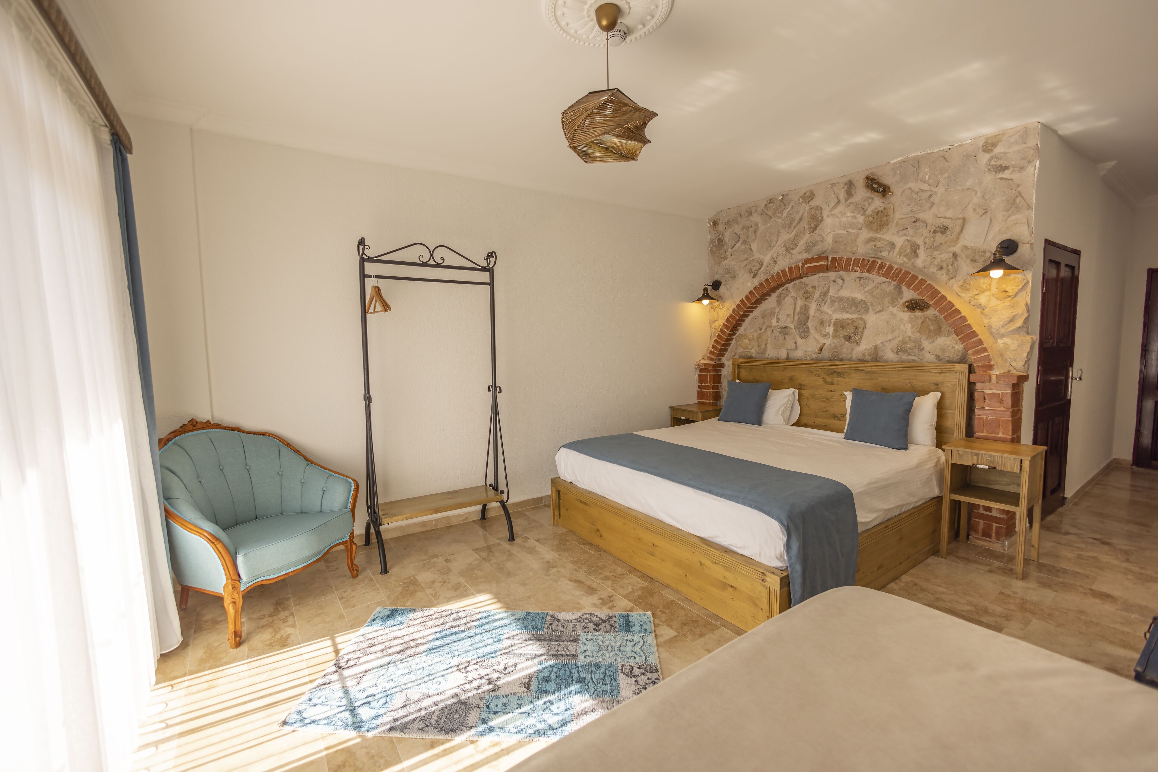 Un dormitorio con una cama grande, cabecera de madera, pared de piedra, una silla colgante y una lámpara de pie.
