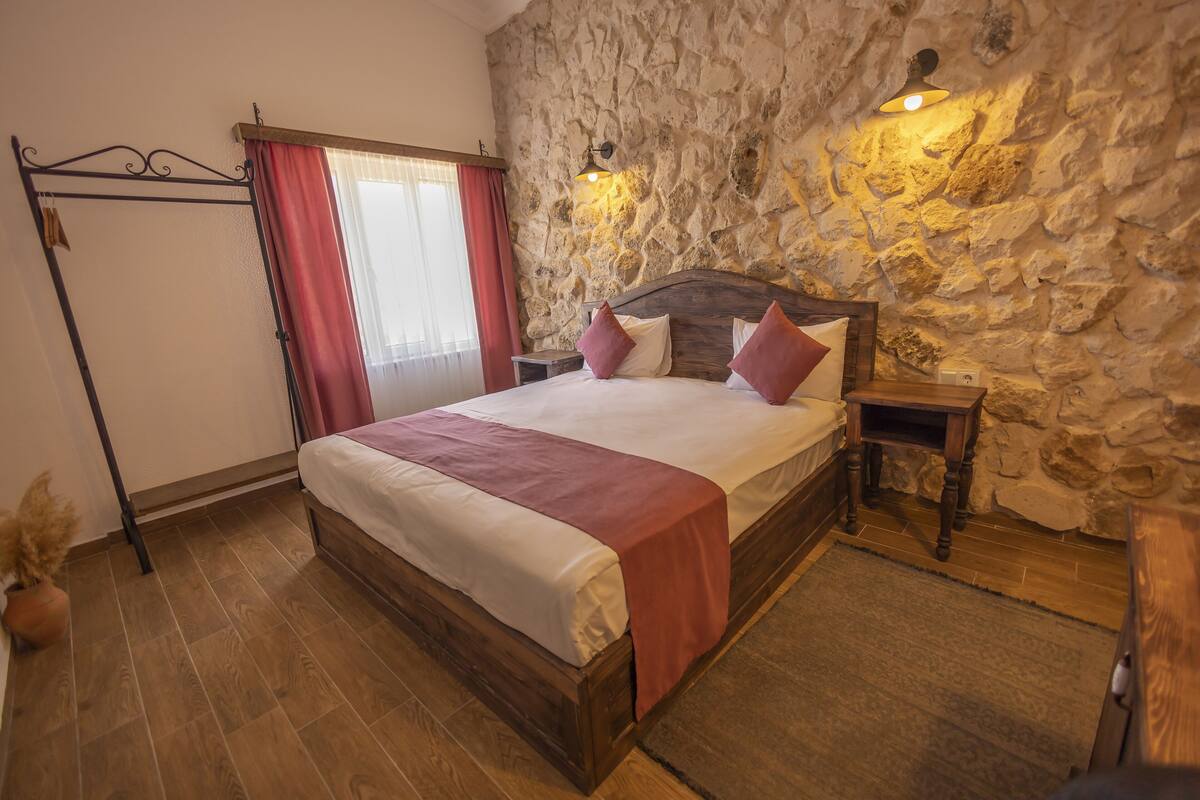 Ein Schlafzimmer mit Steinwand, einem hölzernen Bett, einem Nachttisch und einem Fenster mit Vorhängen.