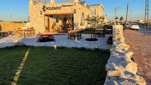 A stone building with a sign reading "SOLEADO Cappadocia." It features outdoor seating and a small garden area. - Soleado Capadocia Hotel (Nevsehir)