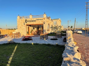 A stone building with a sign reading "SOLEADO Cappadocia." It features outdoor seating and a small garden area. - Soleado Capadocia Hotel (Nevsehir)