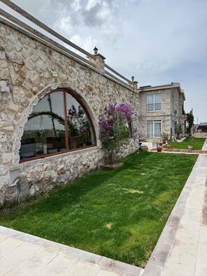 Un edificio de piedra con un amplio ventanal de arco y un pequeño árbol con flores moradas.