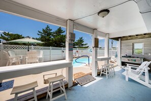 A covered outdoor area with a pool, white Adirondack chairs, and a wooden deck. - Good Day Sunshine-Oceanside, pool, hot tub, dog friendly, close to the beach! (Nags Head)