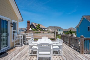 A wooden deck with a white table and chairs, overlooking a residential area with houses and a clear sky.