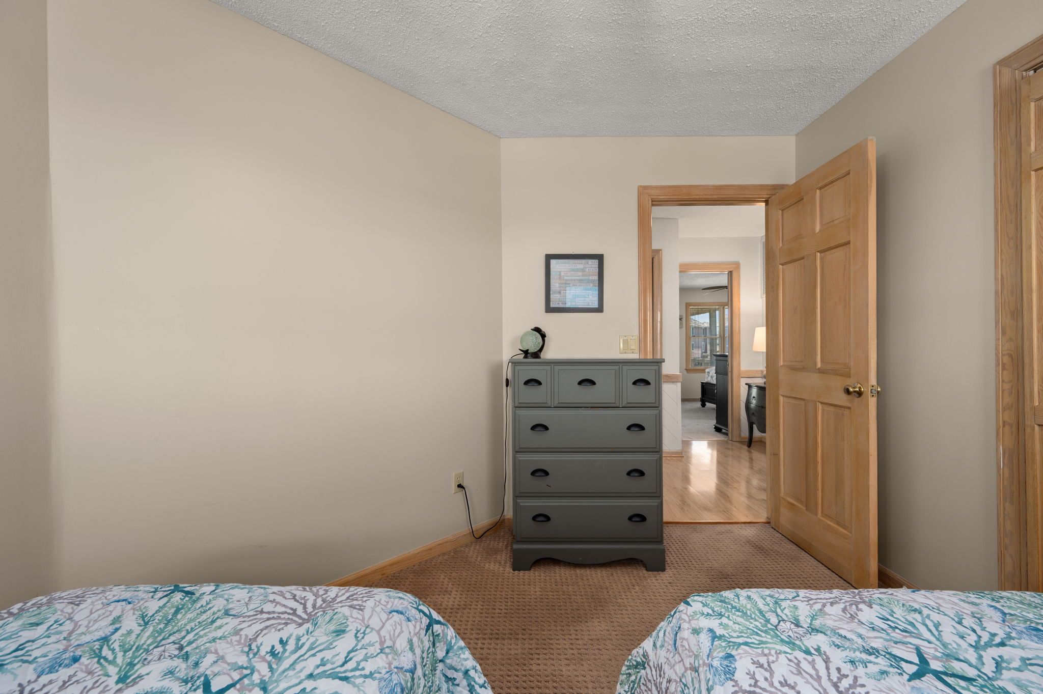 A bedroom with two beds, a dresser, a framed picture on the wall, and a door leading to another room.
