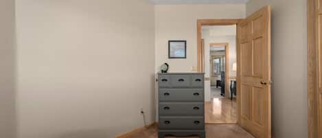 A bedroom with two beds, a dresser, a framed picture on the wall, and a door leading to another room.