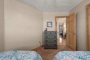 A bedroom with two beds, a dresser, a framed picture on the wall, and a door leading to another room.