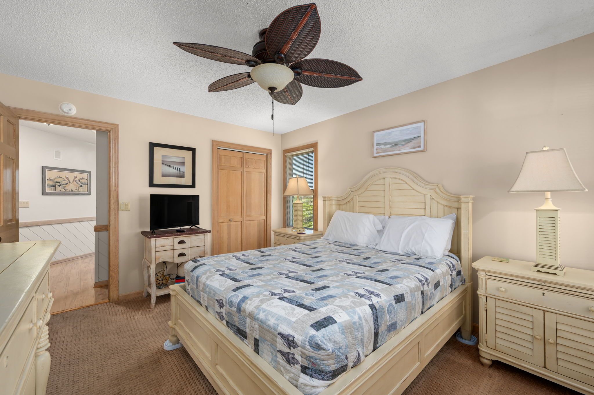 A bedroom with a bed, a ceiling fan, a television, a dresser, and a nightstand.