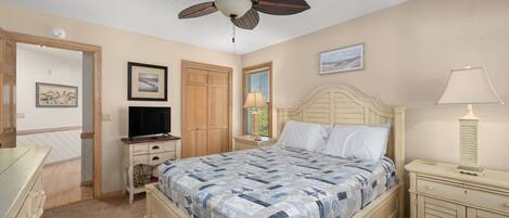A bedroom with a bed, a ceiling fan, a television, a dresser, and a nightstand.