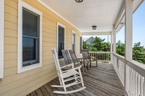 A covered porch with wooden flooring, white railings, and two rocking chairs.