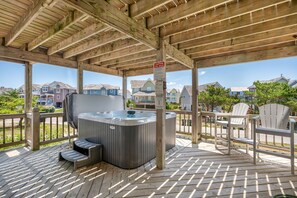 Una terraza de madera con un jacuzzi, asientos al aire libre y vistas a edificios residenciales.