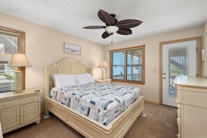 A bedroom with a bed, bedside tables, a ceiling fan, a window, and a door.