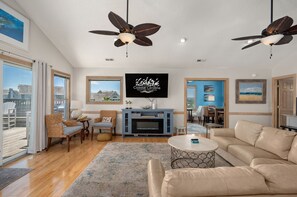 A spacious living room with a large TV, ceiling fans, a fireplace, and a view of the city.