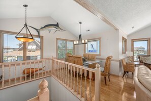 A spacious living area with a dining table, wicker chairs, a sofa, and a staircase with a railing. - Good Day Sunshine-Oceanside, pool, hot tub, dog friendly, close to the beach! (Nags Head)