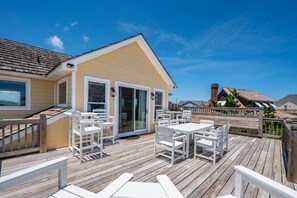 A wooden deck with outdoor seating and a building with a yellow facade.