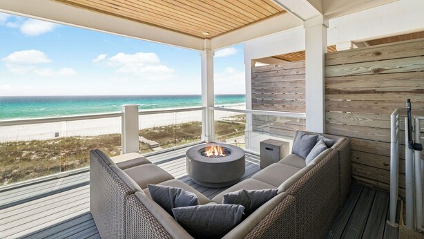 A deck with a fire pit, wicker furniture, and a view of the beach. - Gulf front retreat with pool, hot tub, & beach service—perfect for family groups (Panama City Beach)