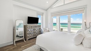 A bedroom with a large bed, a dresser, a television, and a view of the ocean. - Gulf front retreat with pool, hot tub, & beach service—perfect for family groups (Panama City Beach)