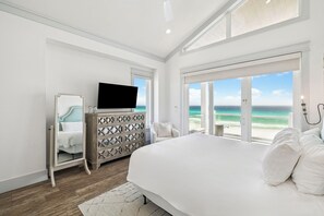 Een slaapkamer met een groot bed, een dressoir, een televisie en uitzicht op de oceaan.