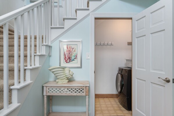 A hallway with a staircase, a laundry area, and a door.