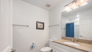 Une salle de bain comprenant des toilettes, un lavabo, un miroir, un porte-serviettes et un tableau encadré au mur.