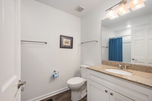 A bathroom with a white toilet, a sink with a granite countertop, a framed picture on the wall, and a blue shower curtain.