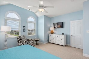 A bedroom with a bed, a dresser, a TV, and two windows.
