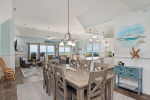 A spacious living area with a large dining table, multiple chairs, and a view of the ocean.