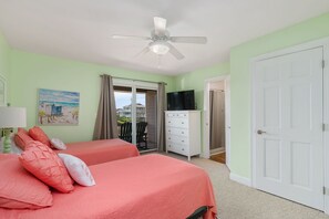 A bedroom with two beds, a ceiling fan, a TV, and a view of the outside.