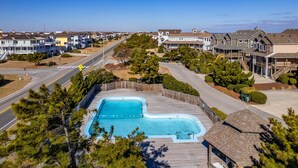 Un quartier résidentiel doté d’une piscine entourée d’une terrasse en bois, de maisons et offrant une vue sur un ciel dégagé.