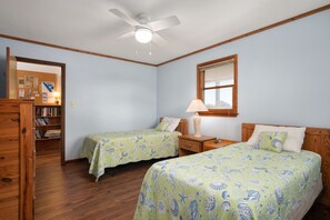 A room with two beds, a ceiling fan, a wooden bookshelf, and a window with blinds. - Tidy Duck-Semi-oceanfront with views, private pool, hot tub, steps to the beach! (Duck)