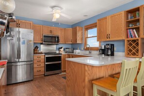 A modern kitchen with wooden cabinets, stainless steel appliances, and a central island. - Tidy Duck-Semi-oceanfront with views, private pool, hot tub, steps to the beach! (Duck)
