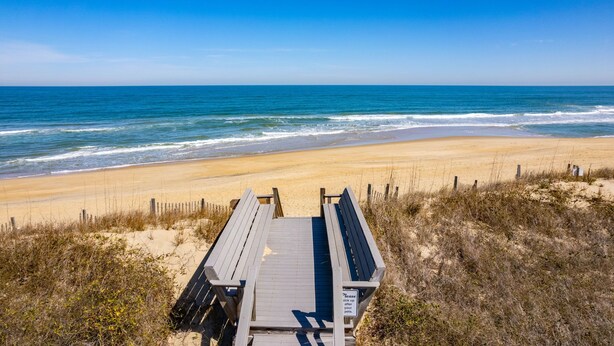 A wooden boardwalk leading to a sandy beach with a clear blue sky and ocean view. - Tidy Duck-Semi-oceanfront with views, private pool, hot tub, steps to the beach! (Duck)