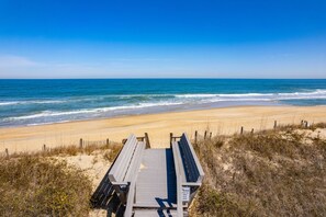 A wooden boardwalk leading to a sandy beach with a clear blue sky and ocean view. - Tidy Duck-Semi-oceanfront with views, private pool, hot tub, steps to the beach! (Duck)