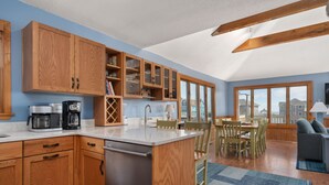 A modern kitchen with wooden cabinets, a built-in island, and a dining area with a view. - Tidy Duck-Semi-oceanfront with views, private pool, hot tub, steps to the beach! (Duck)