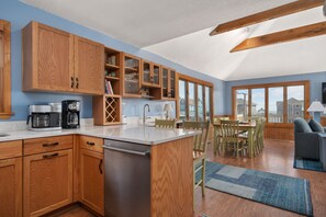 A modern kitchen with wooden cabinets, a built-in island, and a dining area with a view. - Tidy Duck-Semi-oceanfront with views, private pool, hot tub, steps to the beach! (Duck)
