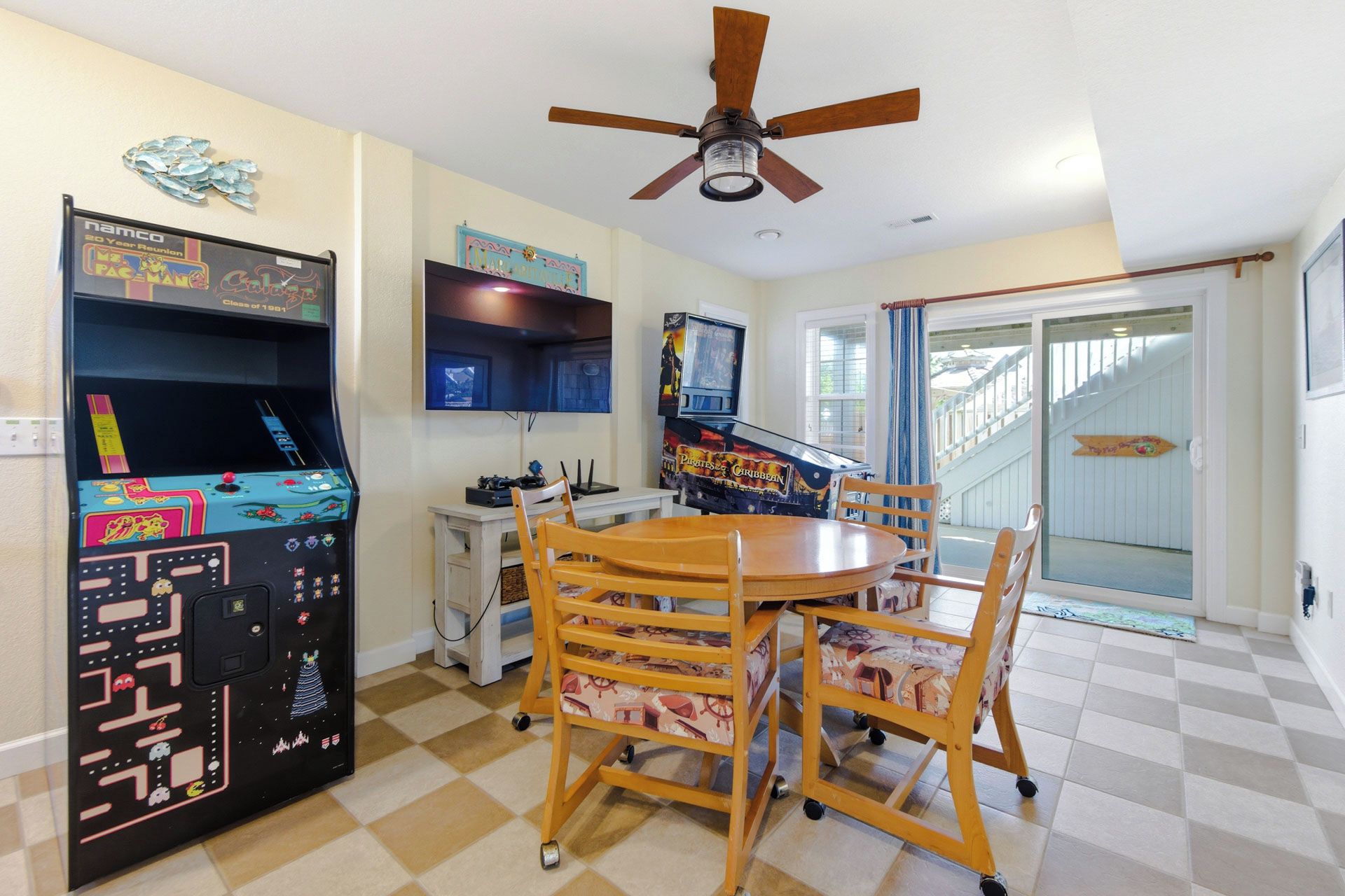 Un espace repas comprenant une table et des chaises, un ventilateur de plafond, des jeux d’arcade et une vue sur l’extérieur.