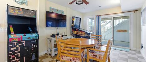 Un espace repas comprenant une table et des chaises, un ventilateur de plafond, des jeux d’arcade et une vue sur l’extérieur.