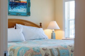 A neatly made bed with white linens, a wooden headboard, and a colorful quilt.
