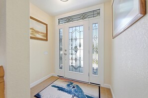 A hallway with a white door featuring decorative glass panels, a framed picture on the wall, and a blue bird rug on the floor. - Queen Anne's Retreat: Oceanside, ocean views, private pool, hot tub & rec room (Nags Head)