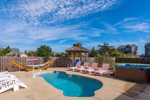 A backyard with a swimming pool, lounge chairs, a hot tub, and a wooden fence.
