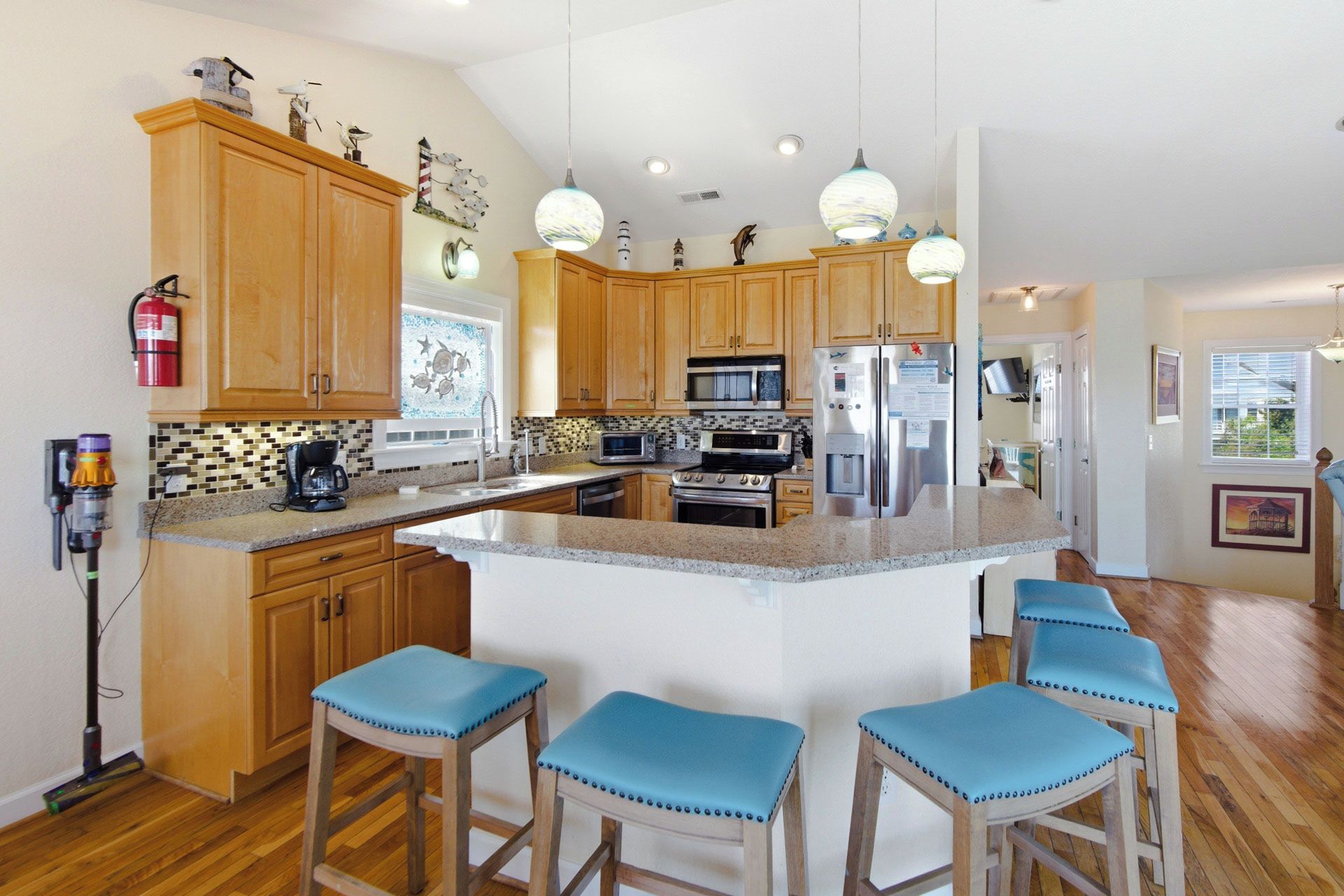 A kitchen with wooden cabinets, a central island with bar stools, a microwave, a refrigerator, and a coffee maker.