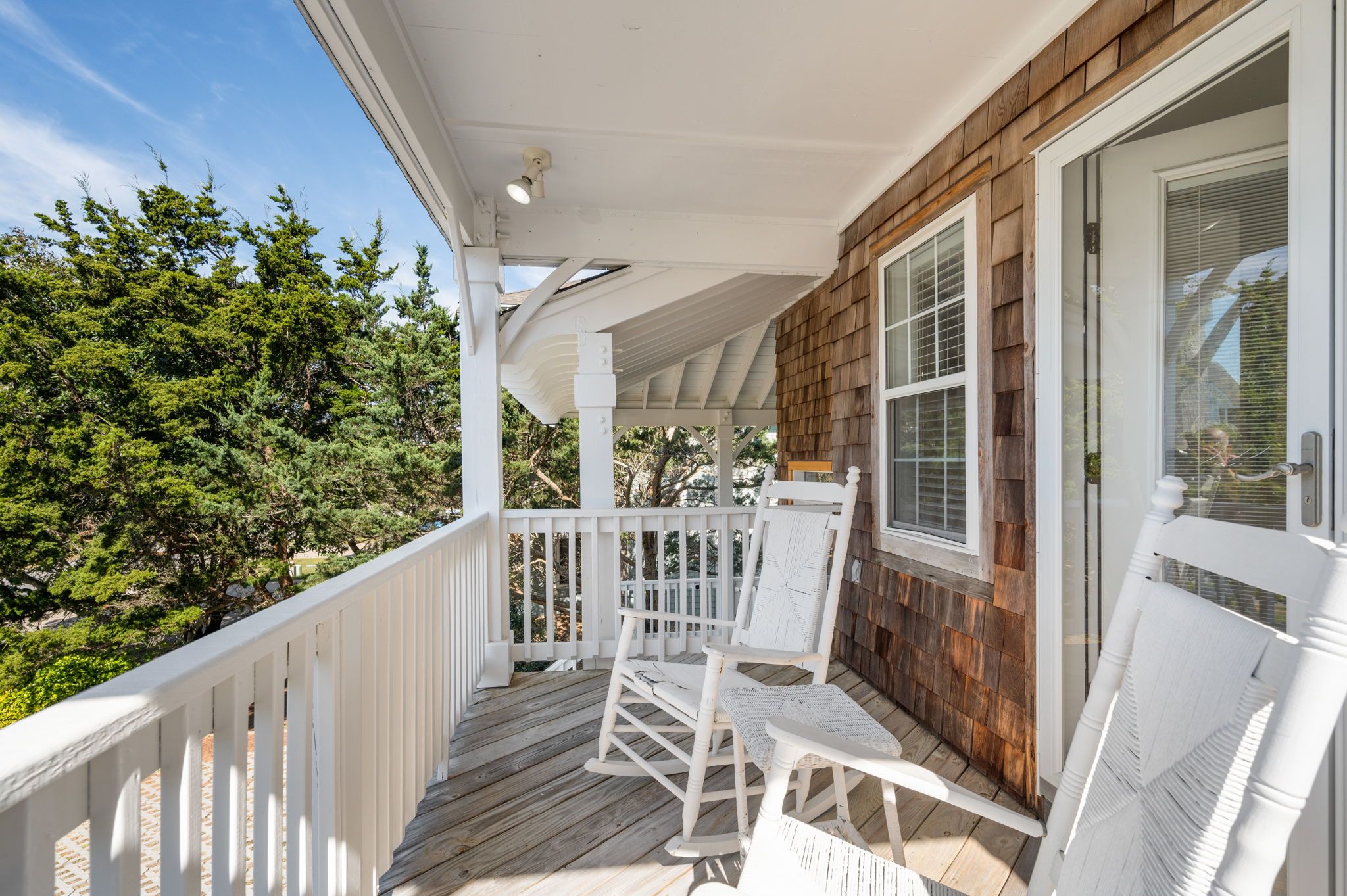 A wooden deck with white railings and two rocking chairs.