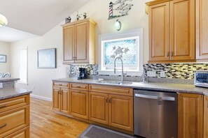 A kitchen with wooden cabinets, a stainless steel dishwasher, a coffee maker, and a decorative window with a mosaic backsplash.