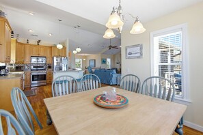 A spacious kitchen with modern appliances, a dining area with a wooden table, and a view of the outdoors through a large window.
